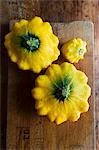 Three yellow patty pan squash on a chopping board (seen from above)