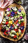 Avocado salad with edible flowers, peppers, red onions and lettuce on a blind-baked pizza base