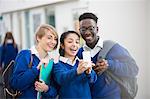 Happy students wearing school uniforms using smartphone in school corridor