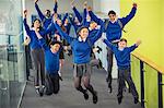 Enthusiastic high school students wearing school uniforms smiling and jumping in school corridor