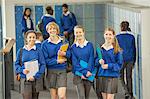 Portrait of smiling female students wearing school uniforms walking through school corridor