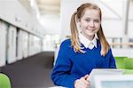 Portrait of smiling elementary school girl with blond pigtails holding digital tablet