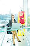 Businesswoman working at office desk with superhero costume behind her