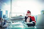 Businesswoman in cape and mask talking on phone at office desk