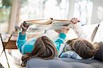 Two girls lying on a sofa on their back, reading a book.