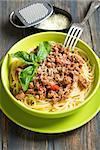 Spaghetti with Bolognese sauce in a green bowl on a wooden table.