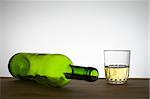 Green wine bottle and a glass of white wine on a wooden table