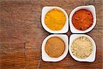 four healthy spices (turmeric, ginger, cinnamon and paprika) in white bowls on a grunge wood