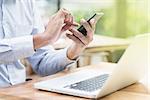 Asian Indian businessman using smartphone and laptop computer at outdoor cafeteria.