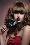 close-up portrait of charming woman with red dress, cute hair-style and black mask in the hand, mysterious style