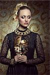 pretty blonde woman in carnival portrait posing with elegant gothic lace dress, baroque jewellery and gold mask. Mysterious masquerade portrait