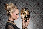 blonde sensual woman with antique gothic carnival dress and baroque jewellery posing with theatrical mask in the hands