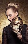 carnival portrait of masquerade blonde woman with antique baroque lady style and venetian mask in the hand. Gothic lace dress and precious jewellery
