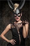 Sexy, beautiful, charming woman in black dress and carnival black rabbit mask in funny pose.