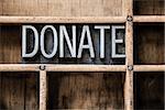 The word "DONATE" written in vintage metal letterpress type sitting in a wooden drawer.