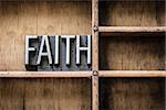 The word "FAITH" written in vintage metal letterpress type sitting in a wooden drawer.