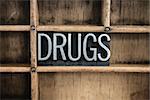 The word "DRUGS" written in vintage metal letterpress type in a wooden drawer with dividers.