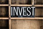 The word "INVEST" written in vintage metal letterpress type in a wooden drawer with dividers.