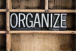 The word "ORGANIZE" written in vintage metal letterpress type in a wooden drawer with dividers.