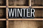 The word "WINTER" written in vintage metal letterpress type in a wooden drawer with dividers.