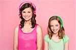 Smiling girls posing with headphone isolated on pink background