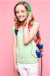 Girl with colorful backpack listening to music. All on pink background