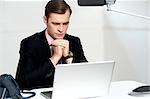 Serious businessman in office concentrating on laptop with hands resting on chin