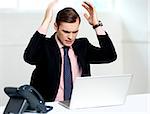 Disappointed businessman looking at laptop with hands above his head