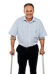 Senior man standing with support of crutches isolated against white background