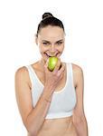 Cheerful healthy fit woman eating fresh green apple isolated over white