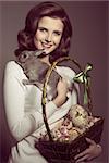 easter portrait of very pretty brunette female with vintage hair-style, posing with lovely fluffy rabbit and basket with colorful eggs