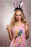 Blonde, beautiful, charming, sexy, woman with bunny ears on the head. She is wearing pink t-shirt and nice makeup.