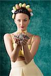 Pretty, brunette woman with funny hairstyle with easter eggs. She wears yellow bra and dress. She is holding some feathers.