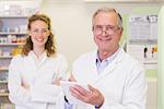 Pharmacist and his colleague with arms crossed behind at pharmacy