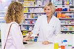 Customer handing a prescription to a smiling pharmacist in the pharmacy