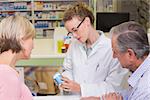 Pharmacist holding a bottle of drugs talking to customer in the pharmacy