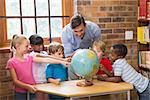 Cute pupils and teacher looking at globe in library at elementary school