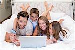 Happy family on the bed using laptop at home in bedroom