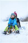 Two girls playing in the snow with sled, winter, Bavaria, Germany