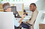 Men sitting at desk in office,talking and smiling