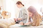 Two teenage girls on bed writting in notepads