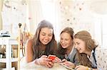 Three teenage girls using smartphone together while lying on bed in bedroom