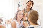 Three teenage girls doing make-up and brushing hair in bedroom