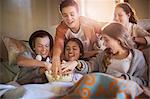 Group of teenagers eating popcorn on sofa in living room