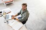 Portrait of young man sitting at desk with mobile phone and laptop