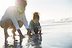 Mother and daughter crouching on beach and touching water