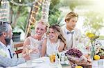 Young couple and their guests sitting at table during wedding reception in garden