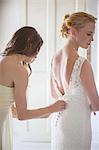 Bridesmaid helping bride with dressing in domestic room