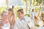 Bridesmaid whispering to bride's ear during wedding reception in domestic garden