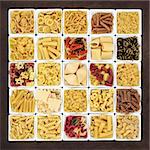 Large pasta dried food sampler in square dishes over brown lokta paper background.